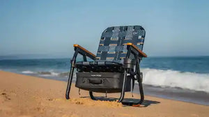 Foldable chair with cooler on a sandy beach with ocean waves in the background