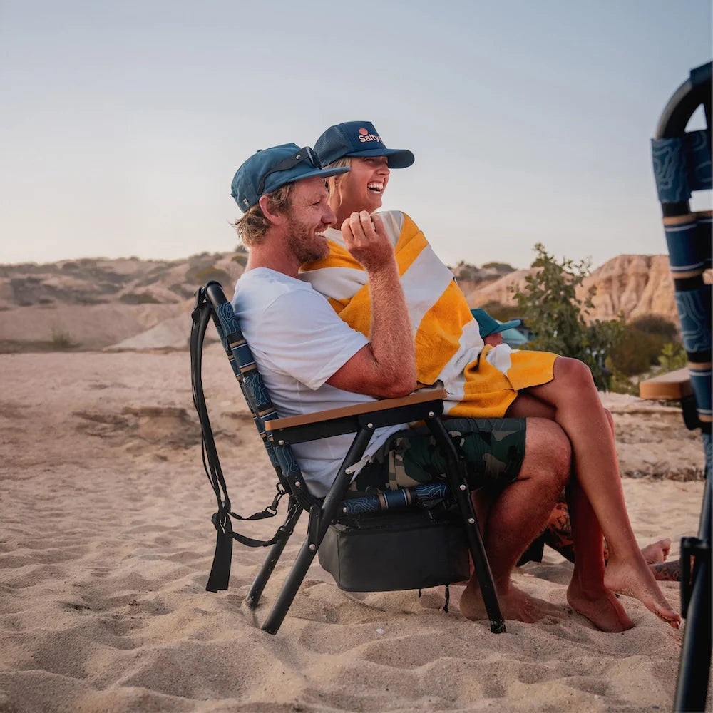 PARKIT x Salty Crew Voyager Chair in limited-edition topo-map pattern, featuring woven webbing, black steel frame, wooden armrests, built-in cooler, cup holder, and backpack straps, rugged 3-in-1 outdoor chair built for surf, fish, and adventure.