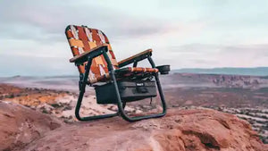 Camping chair with patterned seat and backrest on a rocky outcrop with a scenic landscape in the background.