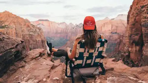 Person sitting in a folding chair wearing a red cap and plaid shirt, overlooking a canyon.